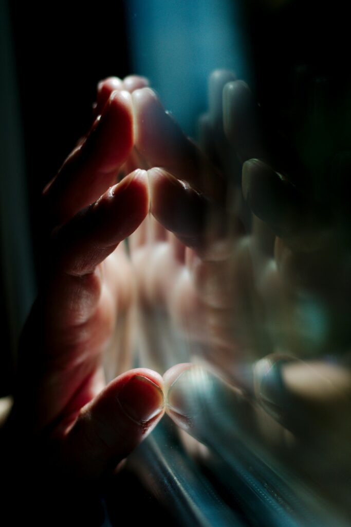 A hand pressing against a glass surface with vivid reflections, creating a moody atmosphere.